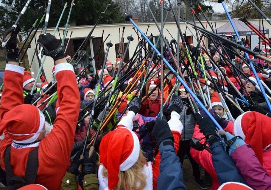 Uczestnicy Nordic walking w czapkach Mikołaja stukający się kijami na powitanie