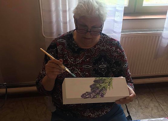 Kobieta siedząca przy stoliku i wykonująca pracę plastyczną