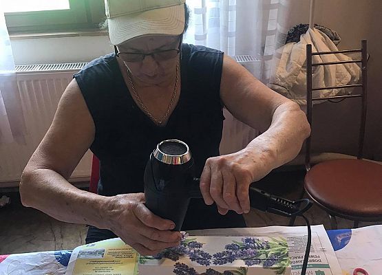 Kobieta siedząca przy stoliku i wykonująca pracę plastyczną