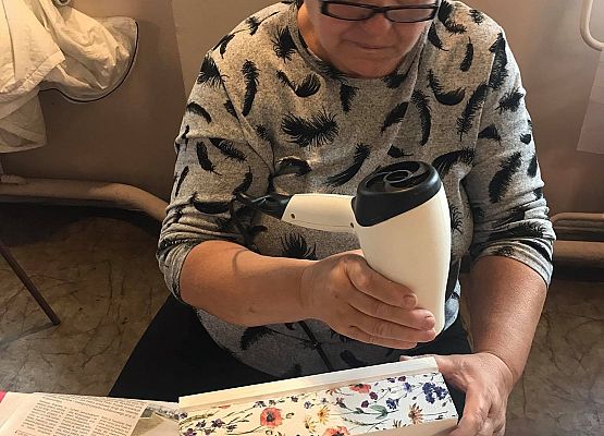 Kobieta siedząca przy stoliku i wykonująca pracę plastyczną