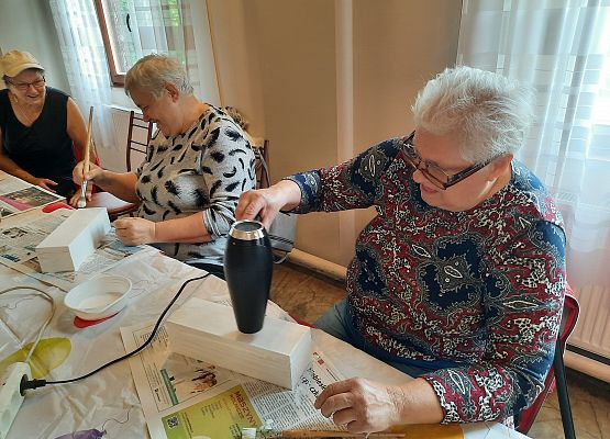 Kobiety siedząca przy stoliku i wykonujące pracę plastyczną