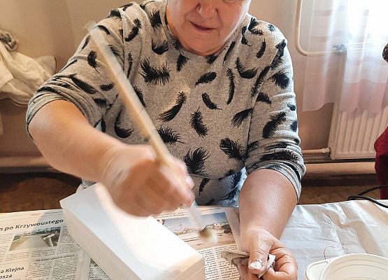 Kobieta siedząca przy stoliku i wykonująca pracę plastyczną