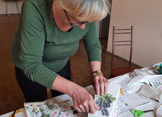 Kobieta siedząca przy stoliku i wykonująca pracę plastyczną