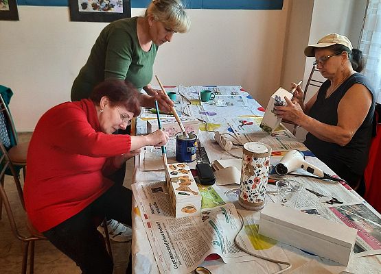 Kobiety siedząca przy stoliku i wykonujące pracę plastyczną