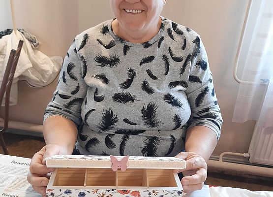 Kobieta siedząca przy stoliku i prezentująca pracę plastyczną