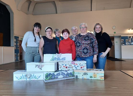 Kobiety stojące obok siębie na tle sali GOK a przd nimi wykonane prace plastyczne