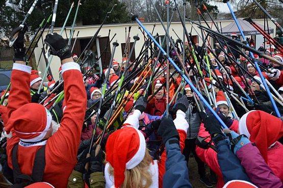 uczestniki Nordic walking w czapkach mikołajowych stukają się kijami na powitanie