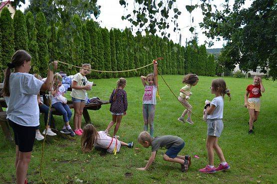Dzieci na podwórku bawią się w przechodzenie pod nisko zawieszoną liną