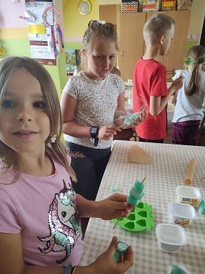 Dziewczynka pozuje do zdjęcia, a w tle jeszcze dwoje dzieci podczas zajęć