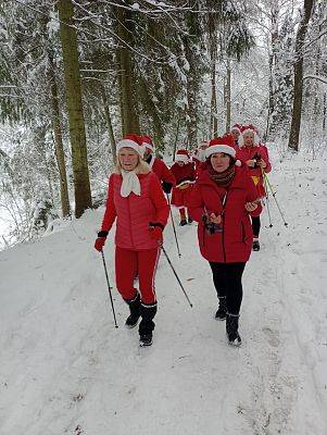 Trzy osoby na tle zimowego lasu  w przebraniach Mikołajowych.