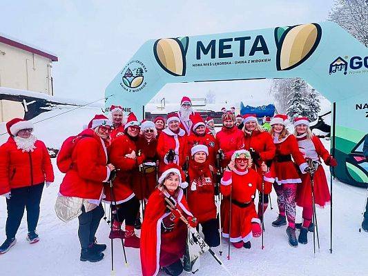 Na tle zimowej scenerii grupa osób w Mikołajowych przebraniach.