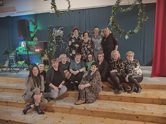 Panie z KGW Lędziechowo i KGW Krępa Kaszubska pozują do wspólnego zdjęcia na tle zielonej dekoracji.