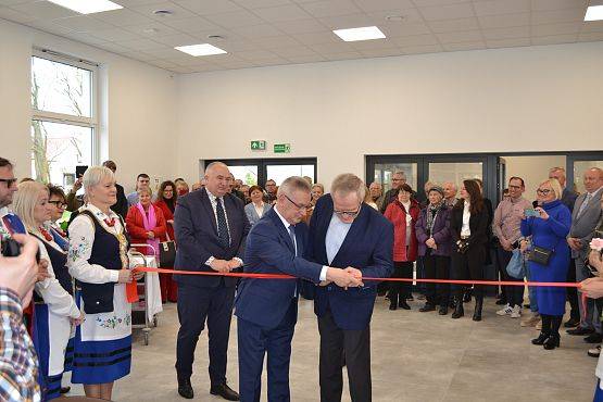 Pan Zdzisław Korda przewodniczący Rady Gminy przecina czerwoną wstęgę, pomaga mu w tym wójt Gminy, w tle pozostali goście na otwarciu.
