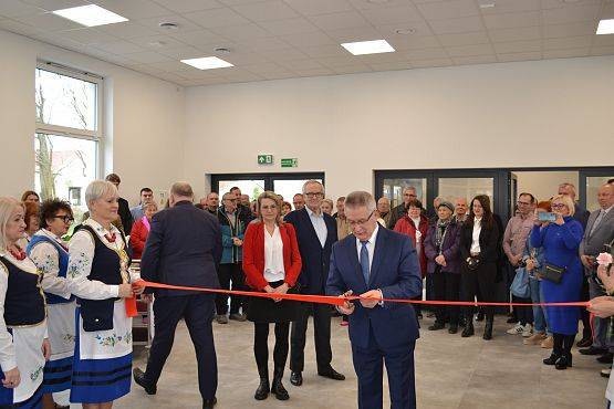 Wójt Gminy Zdzisław Chojnacki przecina czerwoną wstęgę, w tle pozostali goście na otwarciu.