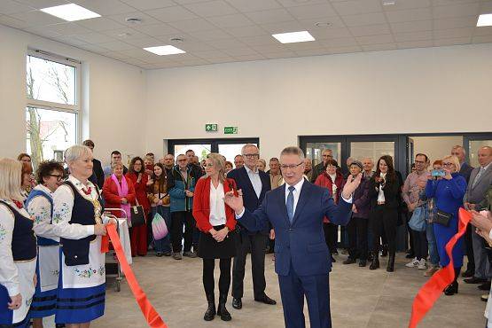 Wójt Gminy Zdzisław Chojnacki przecina czerwoną wstęgę, w tle pozostali goście na otwarciu.