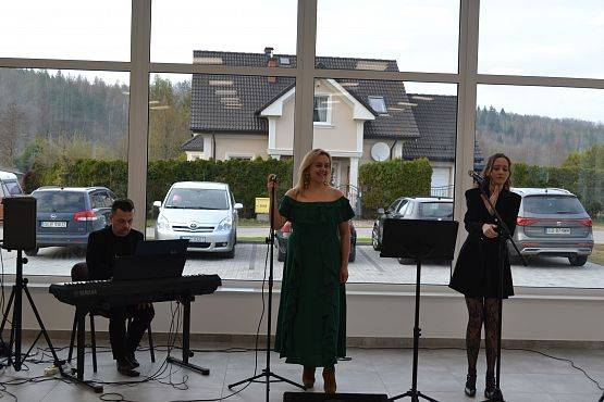 Na tle okien sali 3 osoby podczas spiewania.