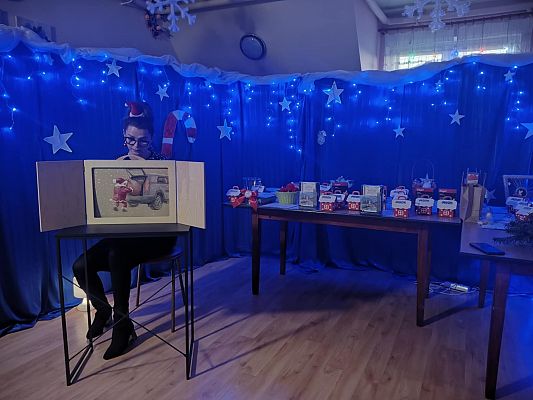 Na tle niebiskiego materiału ozdobionego święcącymi lampkami, Pani Dyrektor czyta dzieciom bajkę.