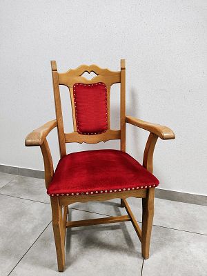 Zdjęcie przedstawia drewniane krzesło z tapicerowanym siedzisku a tle białej ściany