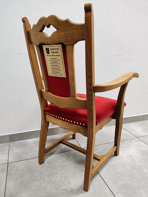 Zdjęcie przedstawia drewniane krzesło z tapicerowanym siedzisku a tle białej ściany